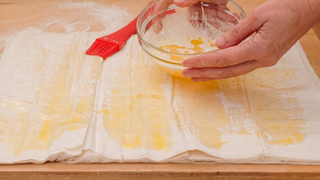 Brush each layer of phyllo dough with melted butter, woman hands