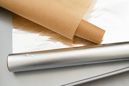 Close-up photograph showcasing essential baking tools including parchment paper, aluminum foil, and a baking pan, ready for use in the kitchenの写真素材