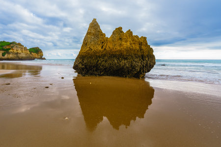 Rugged shoreline with rocky cliffs meeting a sandy beach under a dramatic overcast sky, Algarve, Portugalの写真素材