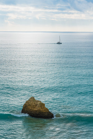 Cliffs meet the powerful Atlantic waves with a distant boat silhouette in the enchanting Algarve, Portugal.の写真素材