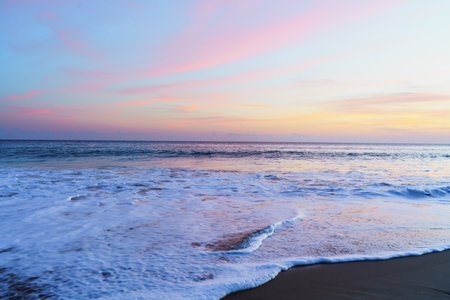 Serene beach scene adorned with the warm hues of a setting sun, casting a mesmerizing glow over the tranquil shorelineの写真素材