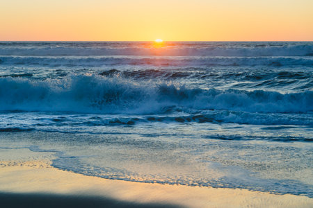 Sea waves glisten under the warm, ethereal light of the setting sun, painting the horizon with a breathtaking blend of fiery oranges and soft blues, tranquil scene, copy spaceの写真素材