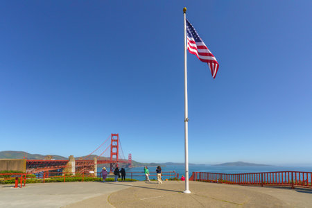 San Francisco, California, April 9, 2024. American flag flying high with the Golden Gate Bridge and visitors in the background.のeditorial素材