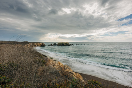 Rocky beach and ocean view at sunset, dramatic cloudy sky in the background, California coastlineの写真素材