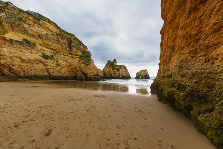 Rugged shoreline with rocky formations, a sandy beach, and a dramatic overcast skyの写真素材