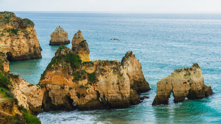 Rugged shoreline with cliffs and caves, set against the backdrop of the Atlantic Ocean's waves crashing on the rocks. Algarve, Portugalの写真素材
