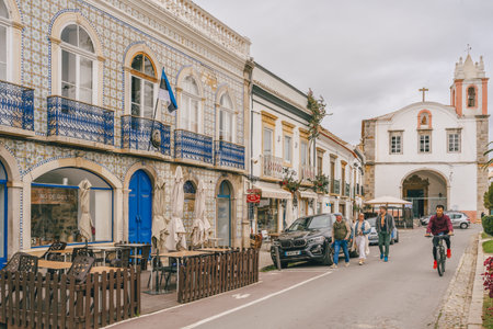 Tavira, Portugal, January 8, 2024. lively street in Tavira, Portugal, with colorful tiled facades, outdoor cafes, pedestrians, and a cyclist riding by.のeditorial素材