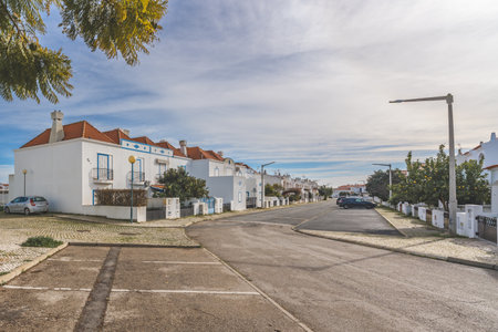Manta Rota, Portugal, January 10, 2024. A residential street in Manta Rota, Portugal, with white houses featuring yellow accents, cobblestone pathways, and lush green trees.のeditorial素材