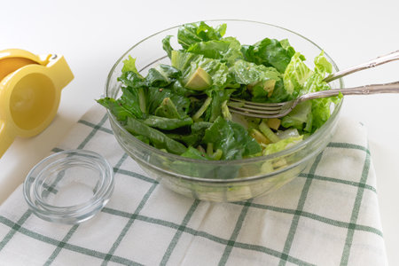 Lettuce salad with fresh avocado, and celery, and lemon olive oil dressing, close-up in a glass bowl on white backgroundの写真素材