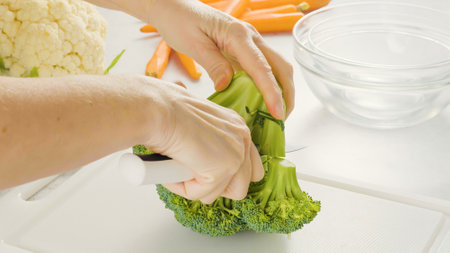 Woman cuts broccoli on a white cutting board. Vegetable soup or salad recipe, preparation processの写真素材