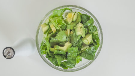 Romaine lettuce, celery, and avocado salad in a glass bowl on white kitchen table, view from above, copy spaceの写真素材