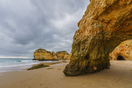 Rugged shoreline with rocky formations, a sandy beach, and a dramatic overcast skyの写真素材