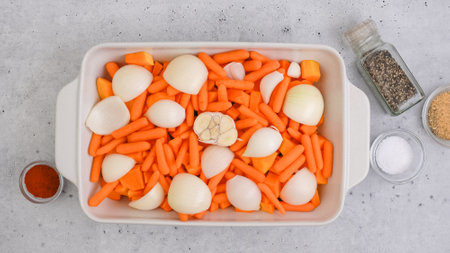 Roasted butternut squash soup recipe. Peeled and seedless squash cubes, carrot, onion, garlic, and spices close-up in a ceramic baking dish on the kitchen tableの写真素材