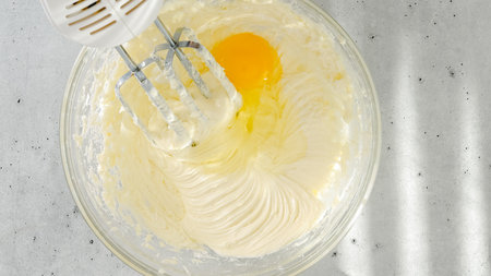 Cream cheese, eggs, and sugar in a bowl. Cheesecake recipe, mixing ingredients in a glass bowl,...