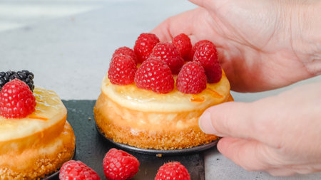 Mini cheesecakes close-up. Topping cheesecakes with orange marmalade, fresh berries, and rosemary, close-up decorating processの写真素材