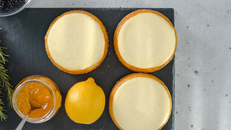 Mini cheesecakes, and ingredients for the dessert topping close-up on kitchen table, flat layの写真素材
