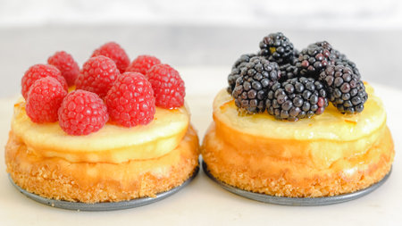 Mini cheesecakes close-up. Topping cheesecakes with orange marmalade, fresh berries, and rosemary, close-up decorating processの写真素材