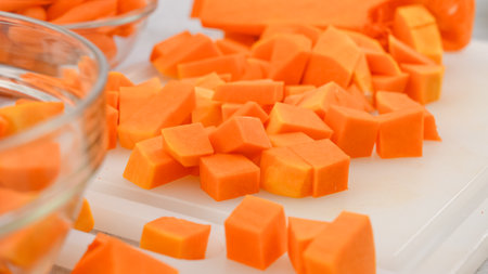 Butternut squash soup recipe. Cubes of a butternut squash close-up on a cutting board on the kitchen tableの写真素材