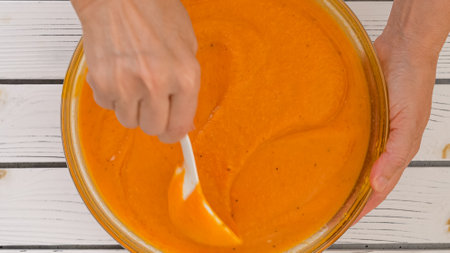 Roasted butternut squash soup recipe, preparation process. Blending roasted vegetables into a puree, adding vegetable stock in a bowl, close-up viewの写真素材