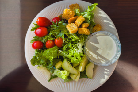 Fresh salad with cucumbers, cherry tomatoes, croutons, and a side of ranch dressing.の写真素材