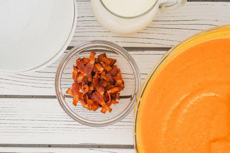 Roasted butternut squash soup served with a crispy bacon and heavy cream topping, close-up in a bowl on a white wooden boardの写真素材