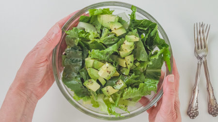 Bowl of fresh green lettuce salad in a woman's hands close-up on white backgroundの写真素材