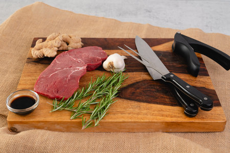 Raw beef steak with ginger root, garlic, soy sauce, and rosemary close-up on a wooden cutting board on the kitchen tableの写真素材