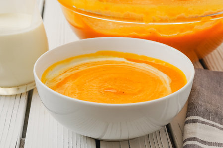 Roasted butternut squash soup served with a crispy bacon and heavy cream topping, close-up in a bowl on a white wooden boardの写真素材