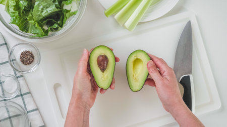 Halves of the avocado in the woman's hands.Green salad recipe, ingredients on white background, flat layの写真素材