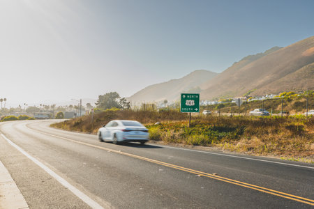 View of California 101 with a car driving under a bright, clear sky along a hilly road.の写真素材