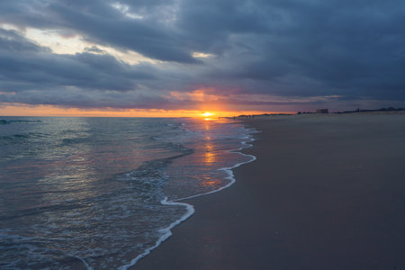 Dramatic sunset skies blaze with color over a peaceful beach, casting reflections on the wet sandの写真素材