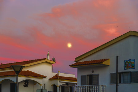 Moonlight shining through colorful evening clouds above suburban homes.の写真素材