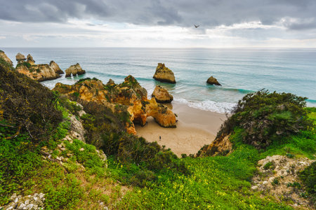 Captivating scene of a rugged shoreline with natural arches and caves, crashing ocean waves, a dramatic beachscape, and a cloudy sky. Algarve, Portugalの写真素材