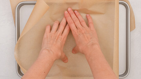 Woman's hands delicately place parchment paper on a baking pan, close-up baking processの写真素材