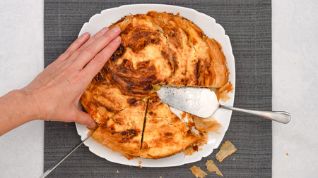 Chef delicately slices through a freshly baked phyllo dough pie, showcasing its golden crust and...