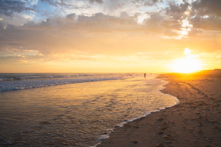 Footprints lead along the shoreline bathed in early morning light.の写真素材