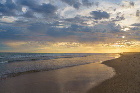 Soft light reflects on the shoreline as evening falls on a tranquil beach.の写真素材