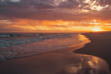 Rich orange and purple hues illuminate the shoreline as the sun sets.の写真素材