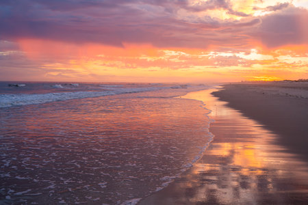 Vibrant sunset colors paint the sky and waves with a warm glow.の写真素材