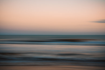Smooth motion of waves reflecting the soft hues of sunset.の写真素材