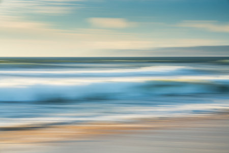 Light airy abstract seascape. Wide sandy beach, sea waves, silhouette of mountains, and cloudy sky in the background, motion blurの写真素材