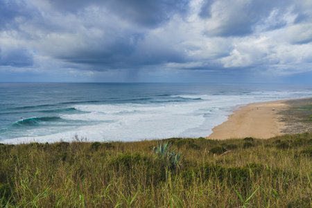 Impending storm casting a dramatic light over the serene and wild Nazare beach.の写真素材