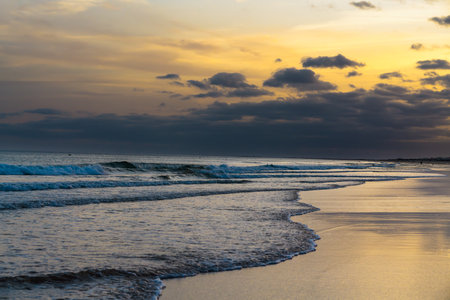 Golden light and dark clouds create a moody seascape at dusk.の写真素材