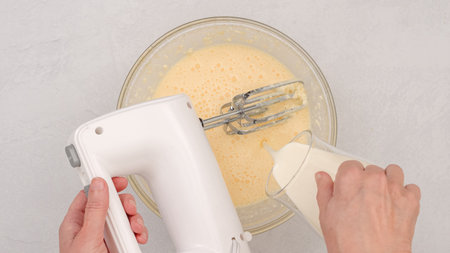 Ingredients like cream cheese, eggs, whipped cream, and powdered sugar mixed with a mixer, flat layの写真素材