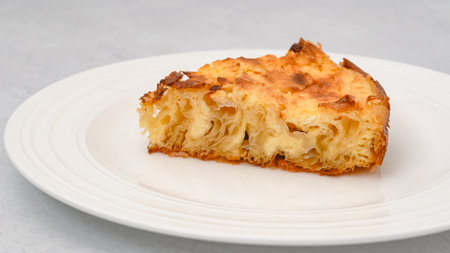 Slice of phyllo dough pie with cream cheese filling close-up on a white plate isolated on a light grey backgroundの写真素材
