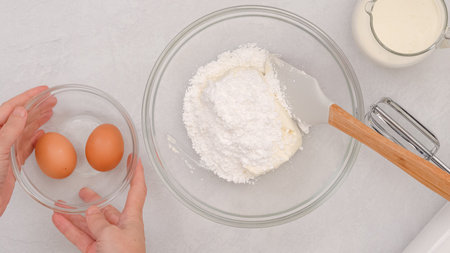 Composition of fresh ingredients like cream cheese, eggs, whipped cream, and powdered sugar, a baking process in motionの写真素材
