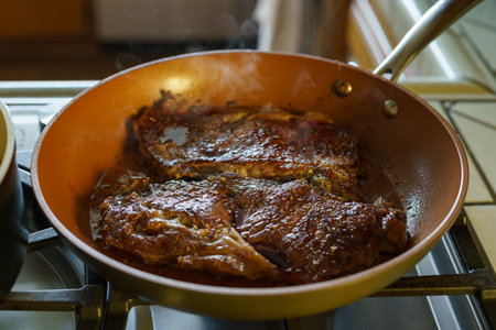 Beef steak close-up, golden-browned and searing in a hot frying pan on the stoveの写真素材