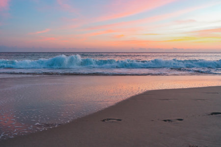 Serene beach scene illuminated by a stunning pink sunset, casting a warm and tranquil glow over the sand and seaの写真素材