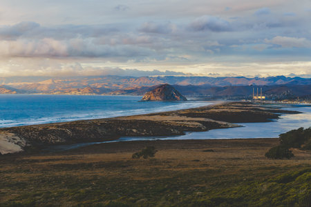 Morro Rock silhouetted against a vibrant sunset, with the cloudy sky adding a touch of drama to the coastal scene, California central Coast.の写真素材