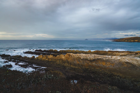 Dramatic scene of a rocky beach at sunset with a cloudy sky in the backgroundの写真素材